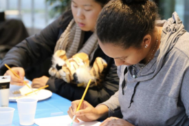 Two participants using their paint brush against a white canvas Two participants using their paint brush against a white canvas